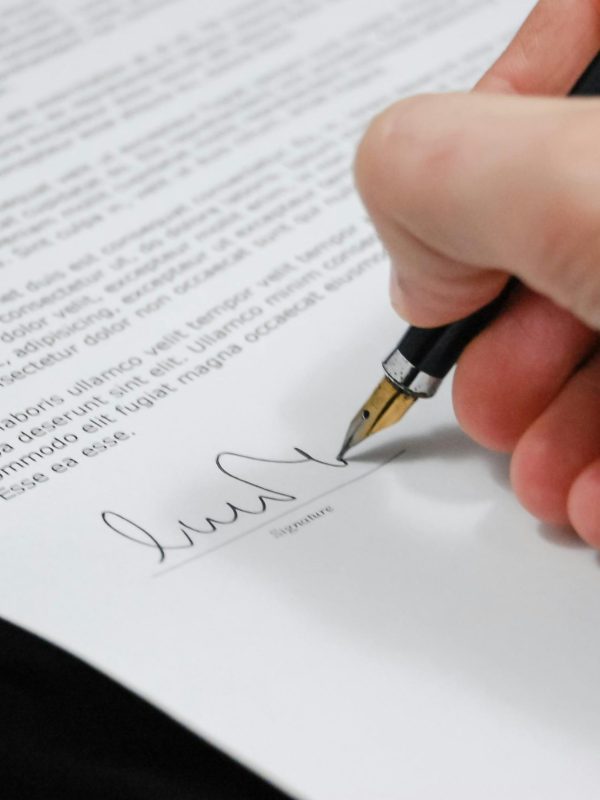 Close-up of a hand signing a legal document with a fountain pen, symbolizing signature and agreement.